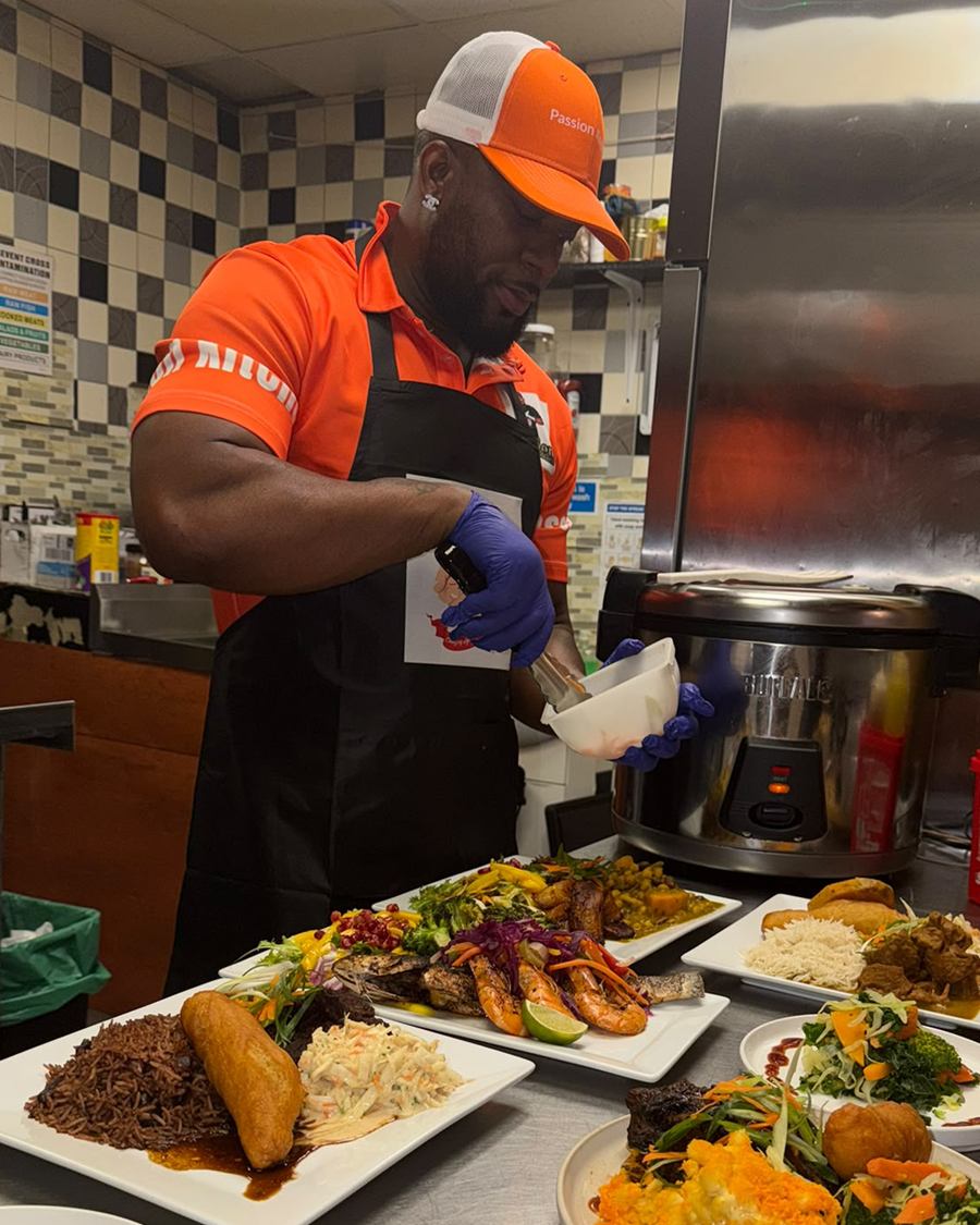Chef Tyrell plating up in the kitchen, spooning sauce over a row of finished dishes on the pass.