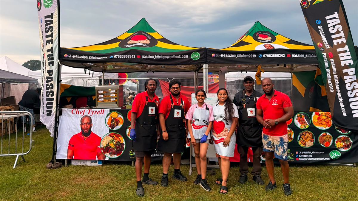 The Passion Kitchen pop-up stall set up on grass, two Jamaican-flag gazebos and the team in red shirts and aprons in front of it.