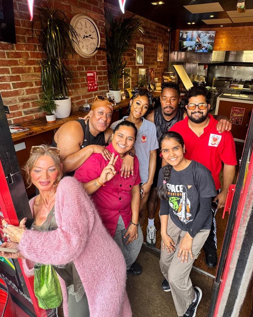 Inside the restaurant — exposed brick, Arsenal pennants and the open kitchen at the back, with staff and customers in the doorway.